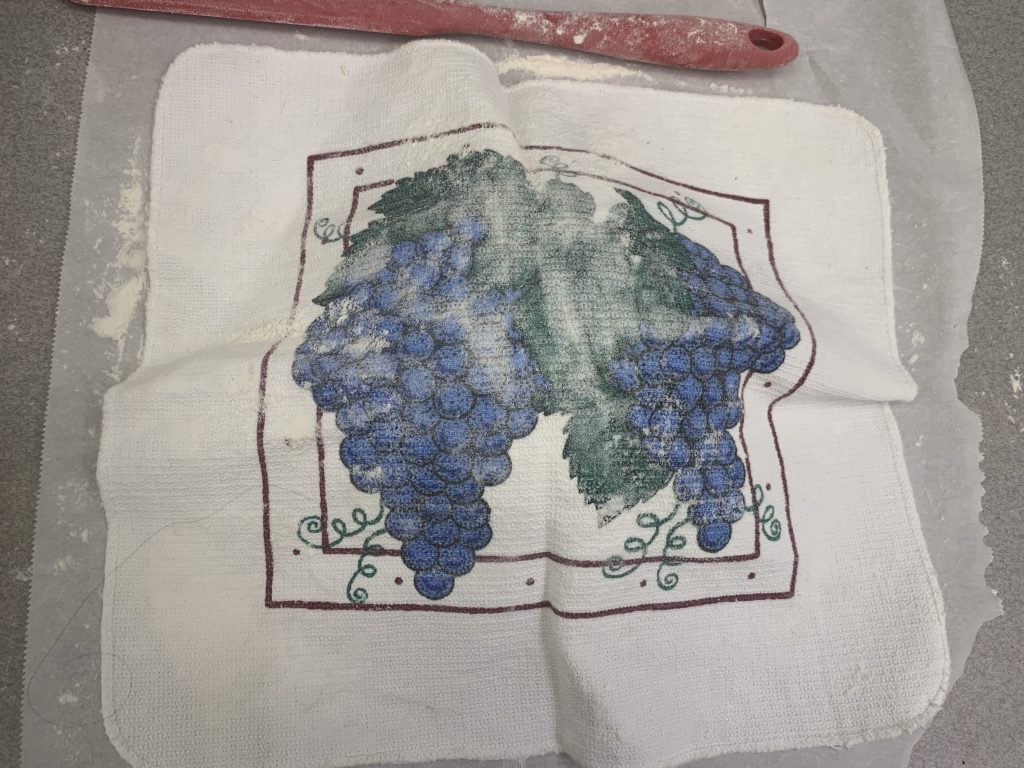 A towel resting on a piece of parchment paper under which is the dough ball.