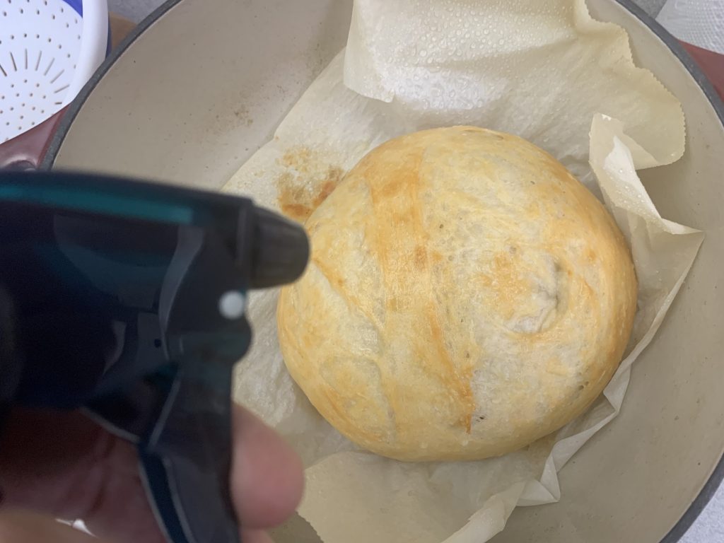 A gently cooked loaf of bread that’s been taken out with a spray bottle of water next to it.
